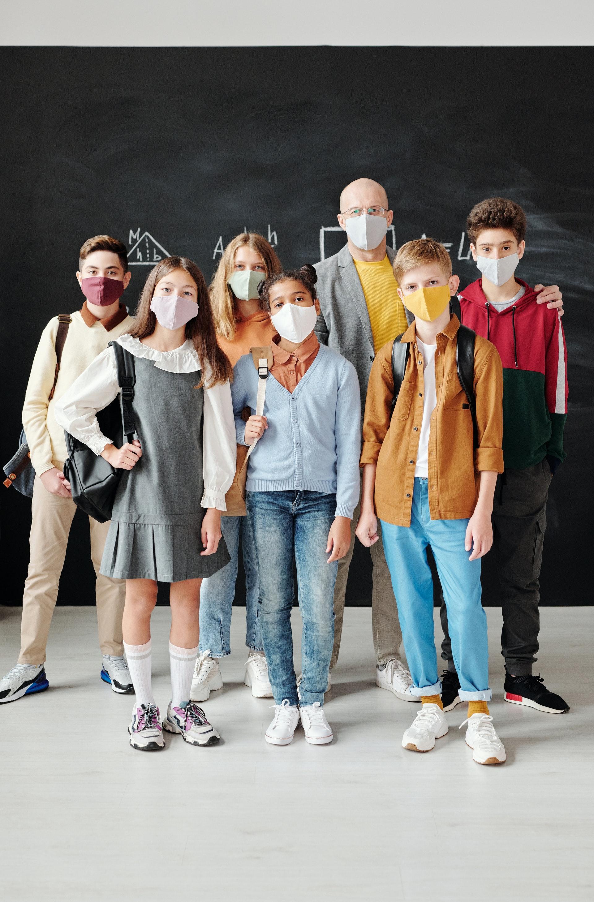 Grupp õpilasi koos õpetajaga tahvli ees - kõigil meditsiinilised maskid ees