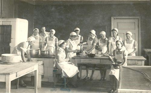 Palju naisi köögis valgete kitlite ja rätikutega  (mustvalge pilt)
